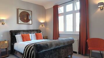 A bedroom with a large bed, a chair, a window with curtains, and wall-mounted lamps.