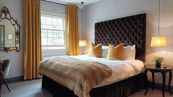 A neatly arranged bedroom with a large bed, two bedside lamps, a round side table with a plant, and a mirror on the wall.