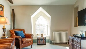 Un salon chaleureux avec un fauteuil en cuir marron, une petite table d’appoint, un radiateur et une fenêtre donnant sur l’extérieur.