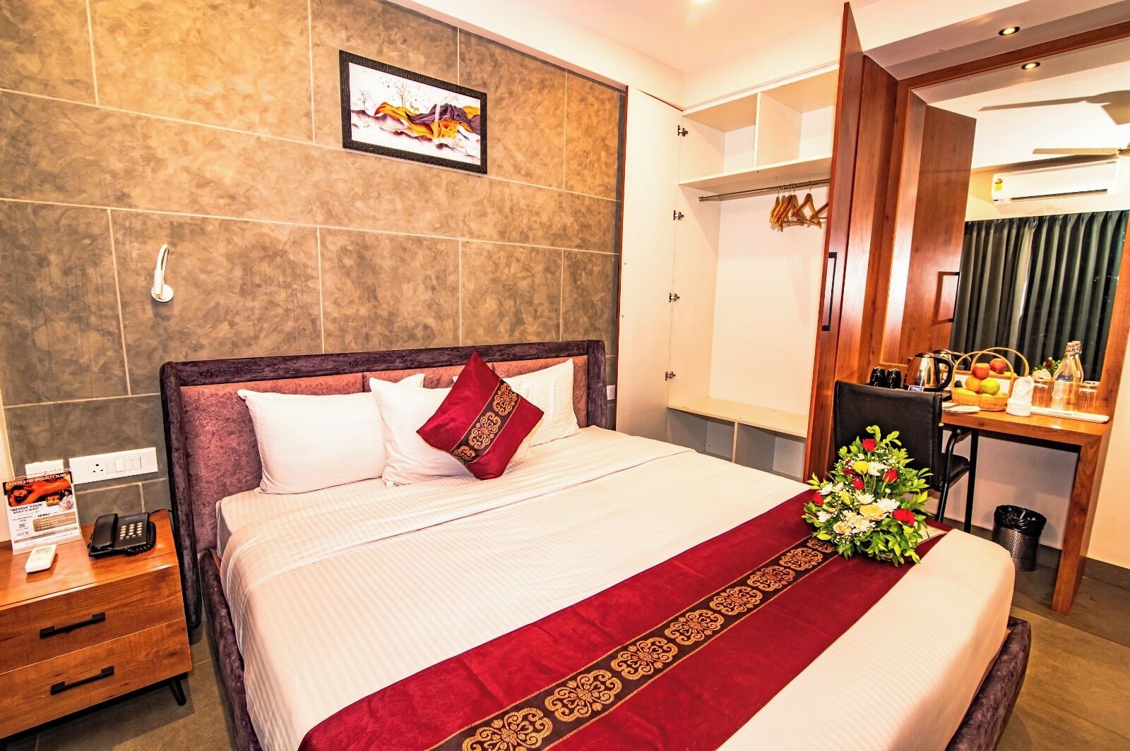 A hotel room with a bed, a bedside table with a phone, a desk with a chair, and a mirror.