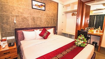 A hotel room with a bed, a bedside table with a phone, a desk with a chair, and a mirror.