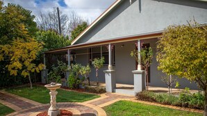 A residential building with a covered porch, a circular brick pathway, and a central garden feature. - The Conductor's Quarters (Bendigo)