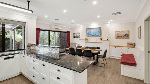 A modern kitchen with white cabinetry, a marble countertop, and a dining area with a wooden table and chairs. - The Conductor's Quarters (Bendigo)