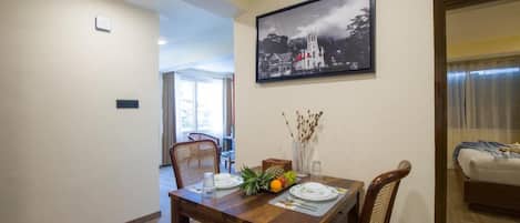 A dining area with a wooden table set for two, a framed black and white photo on the wall, and a view into another room.