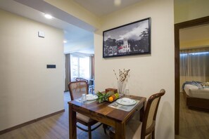 A dining area with a wooden table set for two, a framed black and white photo on the wall, and a view into another room.