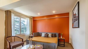 A hotel room with a bed, a chair, a table with a tray, and a window with curtains.