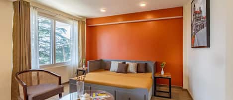 A hotel room with a bed, a chair, a table with a tray, and a window with curtains.