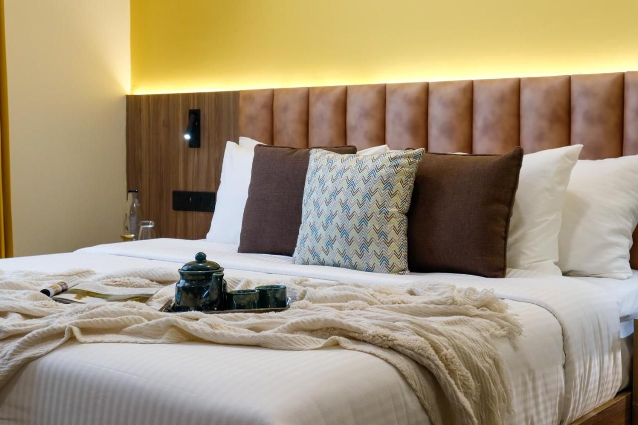 Una cama bien hecha con cabecera de madera, una bandeja con tetera y un cojín estampado.