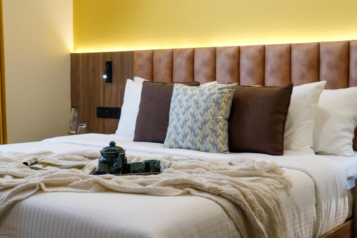 Una cama bien hecha con cabecera de madera, una bandeja con tetera y un cojín estampado.