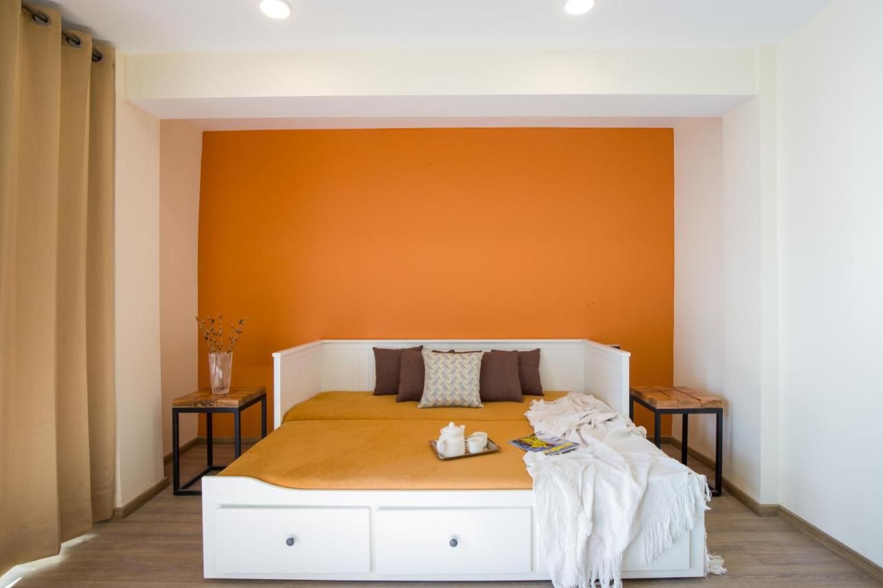 A bedroom with a white bed, orange accent wall, and a small table with a vase.