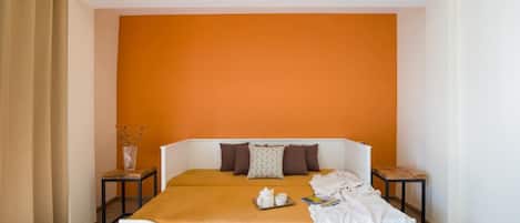 A bedroom with a white bed, orange accent wall, and a small table with a vase.