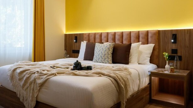 A hotel room with a large bed, wooden headboard, bedside tables, and a window with curtains.