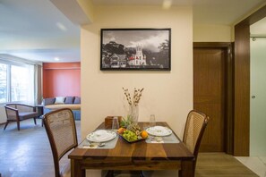 Un comedor con una mesa de madera, dos sillas, un frutero y un cuadro en la pared.