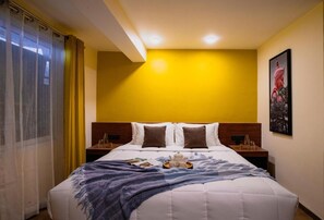 Una habitación de hotel con una cama grande, un cabecero de madera, una mesita de noche con una lámpara y un cuadro enmarcado en la pared.