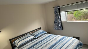 Un dormitorio con cama, ventana con cortinas, una mesita y un calentador de pared.