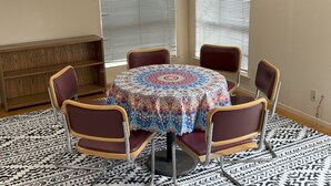 Una mesa redonda con mantel estampado, rodeada por seis sillas de madera con asientos acolchados.