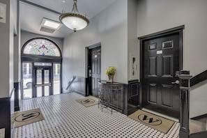 A hallway with a black and white tiled floor, a chandelier, a door with a '101' sign, and a stained glass window.
