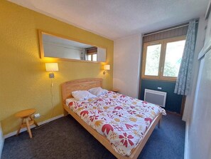 A single bed with a floral bedspread, a nightstand, a wall-mounted mirror, and a window with curtains.