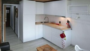 Une cuisine compacte avec des meubles blancs, un plan de travail en bois et un évier. On y trouve une petite table en bois sur laquelle est posé un objet décoratif.