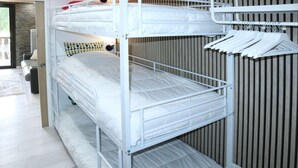 Un lit superposé avec une literie blanche et une structure en métal, une chaise blanche et un mur à rayures verticales.