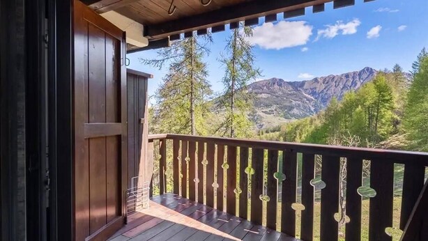 Un balcon en bois offrant une vue sur les montagnes et les arbres.