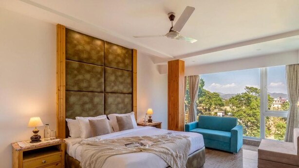 A bedroom with a large bed, a nightstand, a blue sofa, and a view of the outdoors.