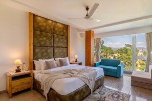 Un dormitorio con una cama grande, una mesita de noche, un sofá azul y vistas al exterior.