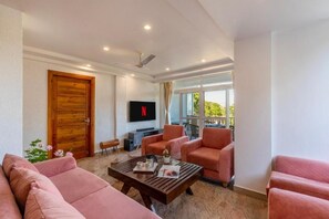 A modern living room with a sofa, armchairs, a coffee table, and a TV mounted on the wall. - Alaya Stays By Elivaas Livelife - Kasauli (Kasauli)