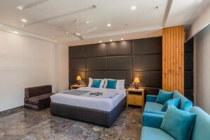 A modern hotel room with a large bed, a wooden accent wall, a sofa, and a nightstand with lamps. - Alaya Stays By Elivaas Livelife - Kasauli (Kasauli)