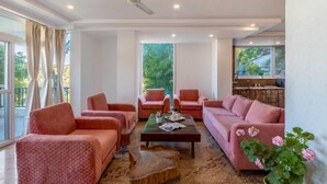 A spacious living room with a large window, a ceiling fan, and a coffee table with a magazine.