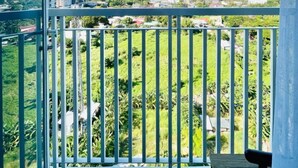 Un balcon doté d’une rambarde en métal, d’où l’on peut admirer un paysage verdoyant et des bâtiments situés au loin.