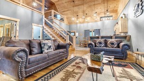 A spacious living area with a high wooden ceiling, two sofas, a coffee table, and a staircase leading to an upper level. - Pinewood Forest: 3BR Cabin with Hot Tub & Game Room (Sevierville)