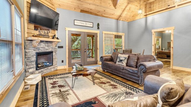 A cozy living room with a stone fireplace, leather sofa, and a dog. - Pinewood Forest: 3BR Cabin with Hot Tub & Game Room (Sevierville)