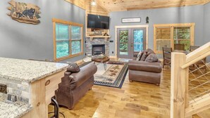 A spacious living room with a stone fireplace, leather sofas, and a large TV. - Pinewood Forest: 3BR Cabin with Hot Tub & Game Room (Sevierville)