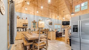 A spacious kitchen with wooden cabinets, a large dining table, and a stainless steel refrigerator. - Pinewood Forest: 3BR Cabin with Hot Tub & Game Room (Sevierville)