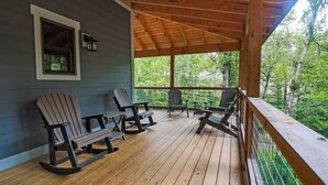 Une terrasse en bois avec des fauteuils à bascule et une table, donnant sur une zone boisée.