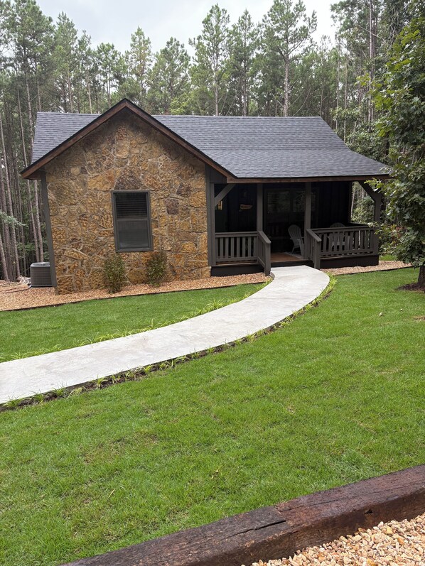 A stone building with a porch and a covered area, surrounded by a well-maintained lawn and trees. - Twisted Pine Cabin in Jasper. Sleeps 2 w/Hot tub & Covered Patio w/gas fireplace (Jasper)