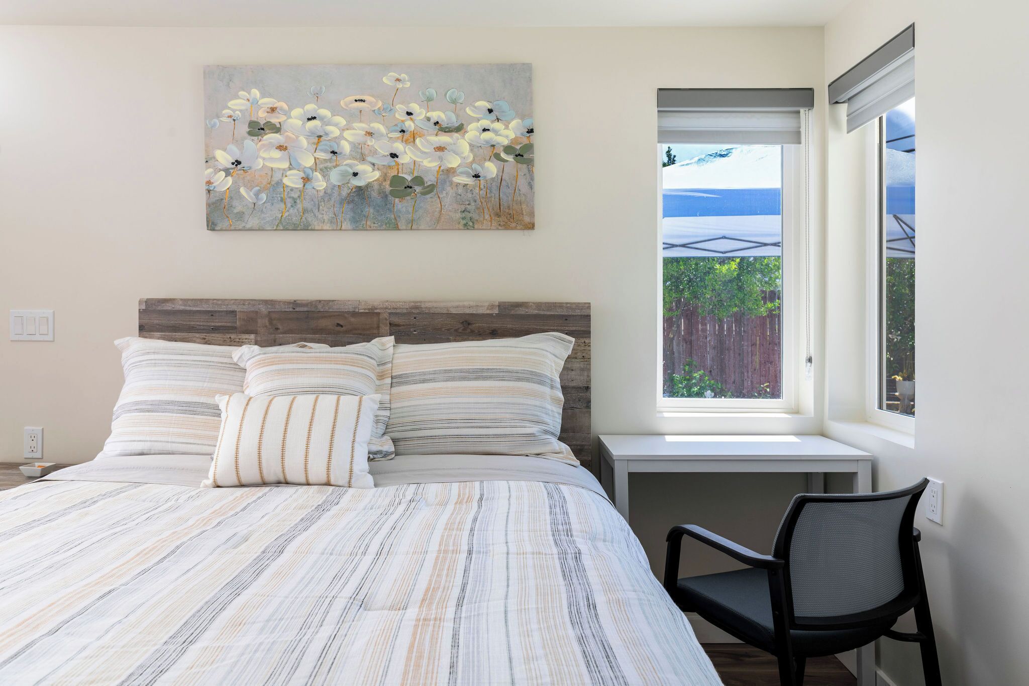 A bedroom with a bed, a chair, a painting, and a window with a view.