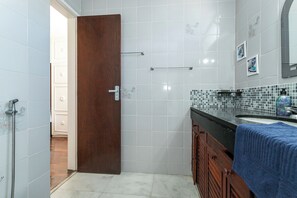 A bathroom with a wooden door, tiled walls, a sink with a blue towel, and a shower area.