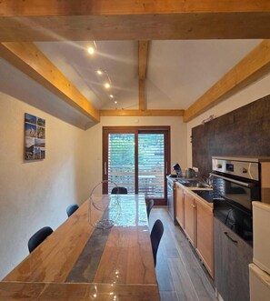 A modern kitchen with wooden beams, a dining table, and a view through the sliding glass doors.
