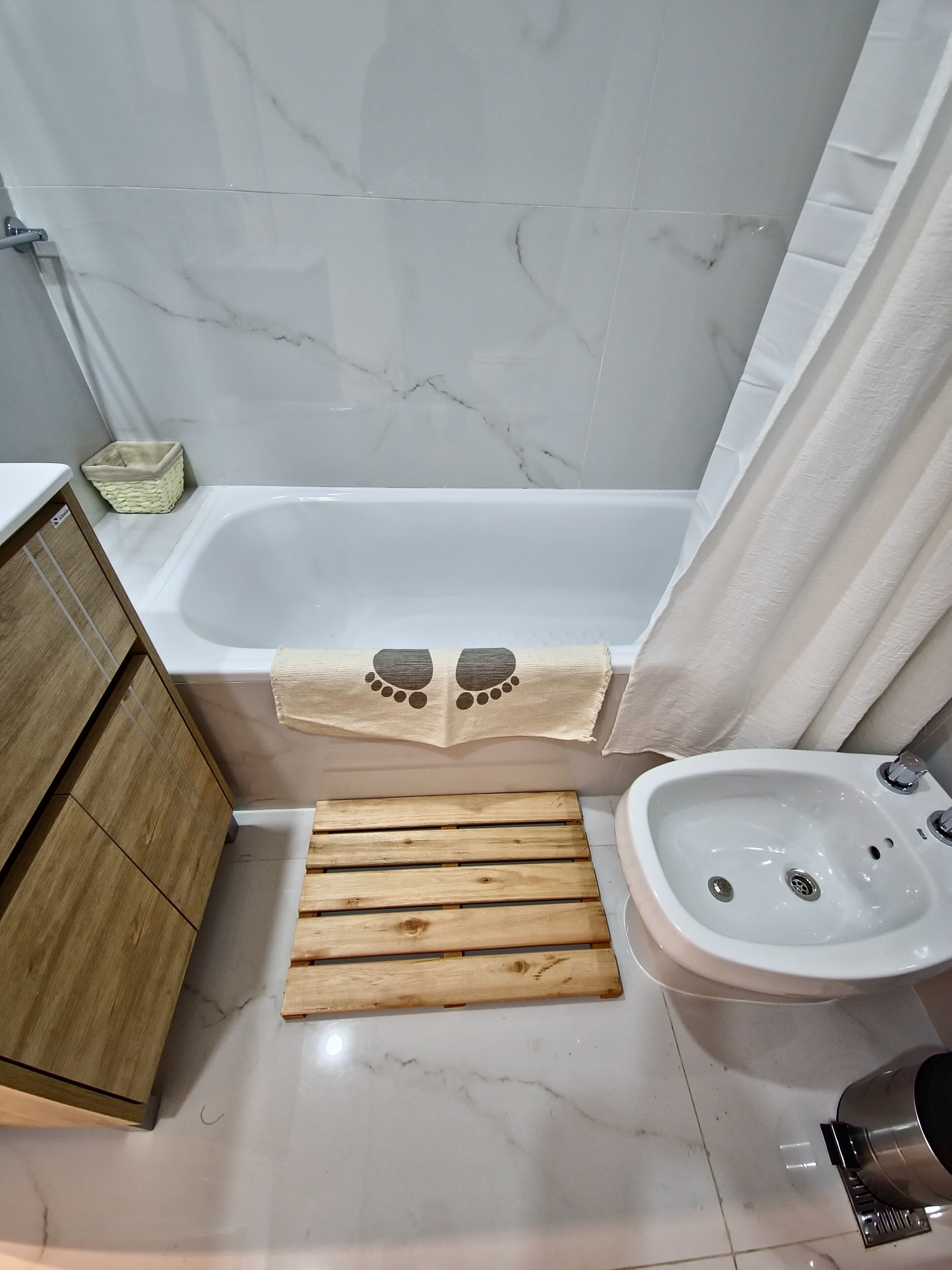 A bathroom with a bathtub, wooden bench, sink, and a small basket.