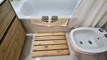 A bathroom with a bathtub, wooden bench, sink, and a small basket.