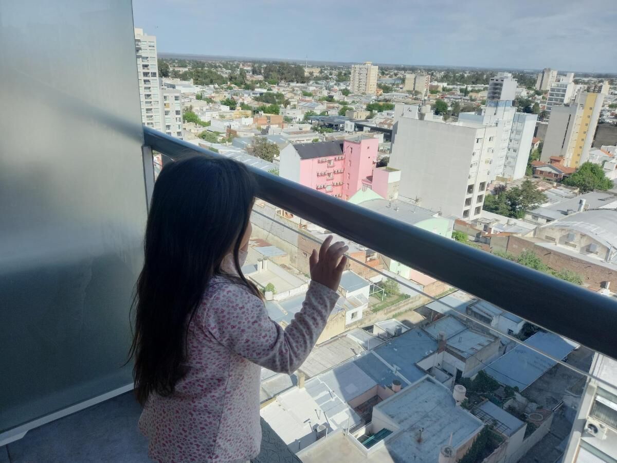 A child standing by a balcony railing overlooking a cityscape with various buildings.