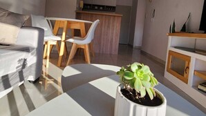 Ein modernes Wohnzimmer mit einer Couch, einem Esstisch mit Stühlen, einer Küchenzeile und einem Blumentopf auf einem weißen Tisch.