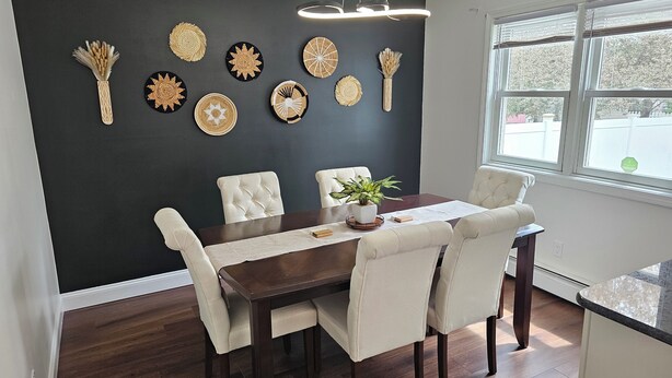A dining area with a dark wall, wooden floor, and a table with chairs. Decorative plates and a plant are on the wall. - Modern Family Retreat w/ Office & Fast WiFi (East Hartford)