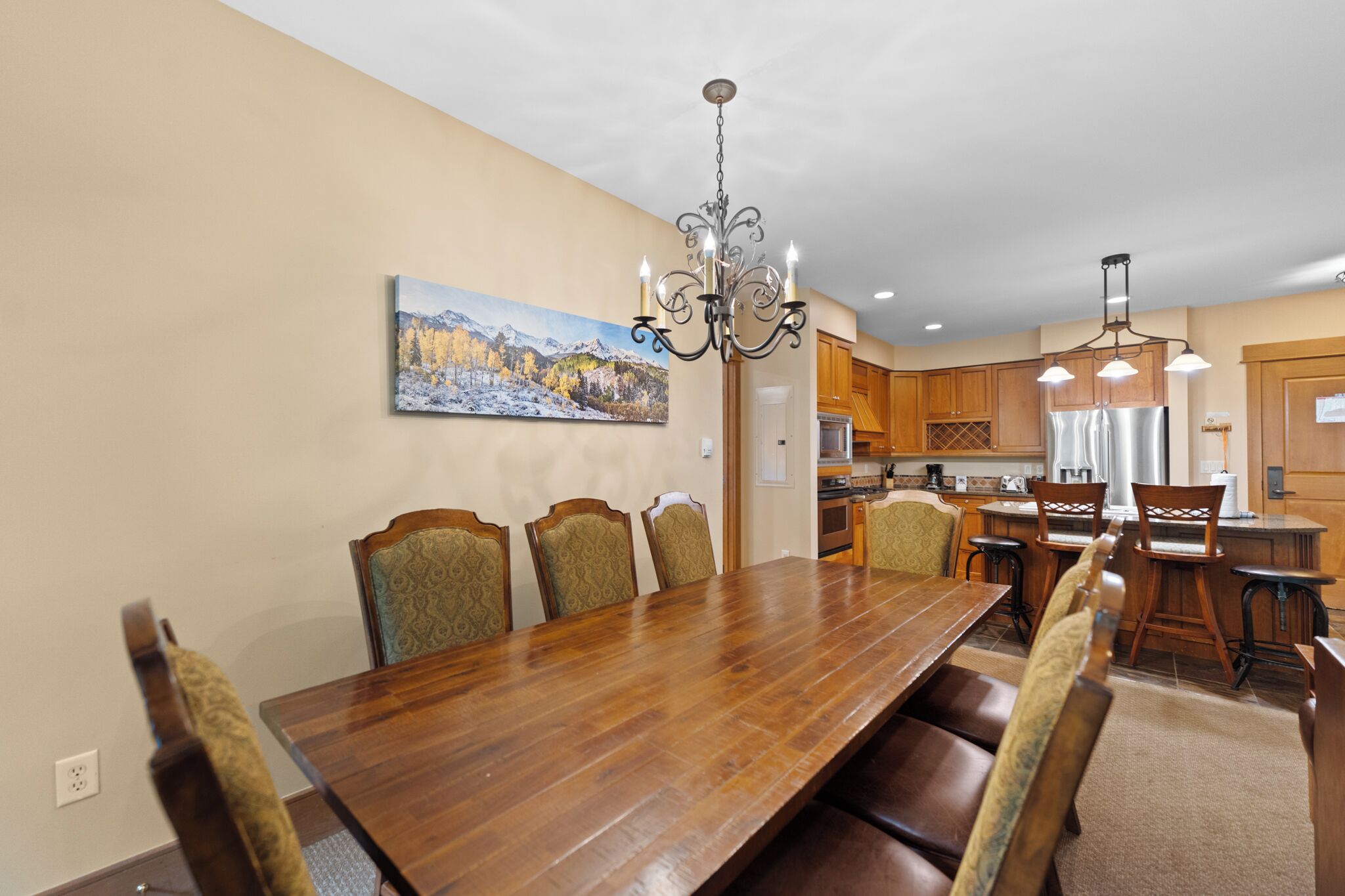 A dining area with a wooden table and chairs, a chandelier, and a painting on the wall.