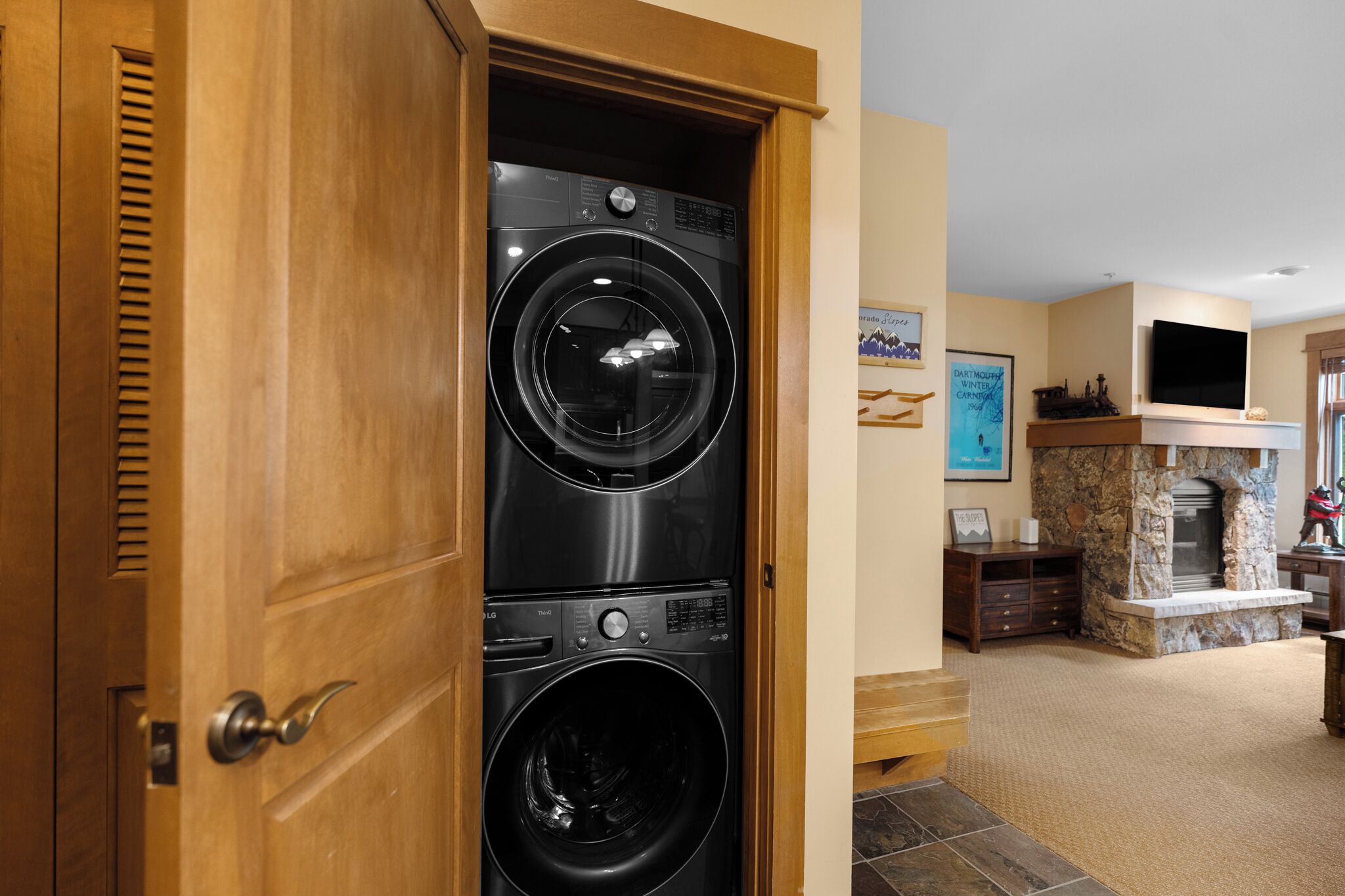 A laundry room with stacked washers and dryers, a stone fireplace, and a television mounted above it.