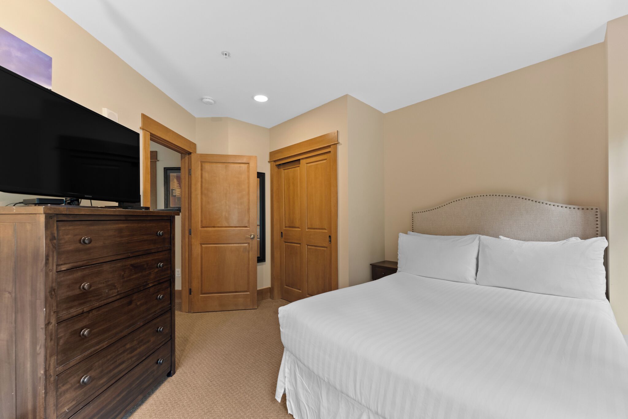 A bedroom with a bed, dresser, television, and wooden doors.