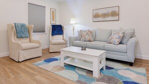 Una sala de estar con un sofá color crema, dos sillones, una mesa de centro blanca y un tapiz estampado.