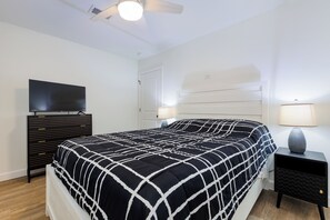 Une chambre à coucher avec un lit, un téléviseur posé sur une commode, deux tables de chevet avec des lampes et un ventilateur de plafond.